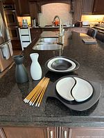 Overview of Japanese serving set items arranged on kitchen countertop: 2 sake servers, serving dishes, chopsticks with stands.