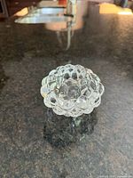 Clear crystal votive candle holder with raspberry-inspired rounded textured design seen from top and side angles on a black countertop