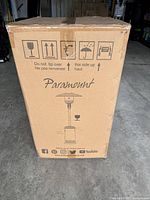 Front of box showing brand Paramount, image of patio heater, precaution icons and social media handles.