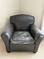 Front view of black leather armchair showing cushioned seat and solid backrest with signs of wear.