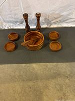 Full set displayed on a dark mat with large salad bowl, four smaller bowls, salt and pepper shakers, and wooden fork and spoon.
