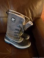 Side view of both boots showing grey suede upper, black rubber lower and fleece lining at opening, positioned on leather surface.