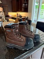 Pair of brown Dakota women's construction boots with black steel toes and thick tread soles on dark countertop.