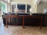 Two matching solid pine wood desks placed side by side behind a sofa with a brown leather couch and lamps on top.