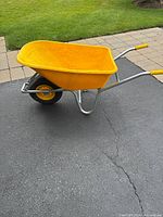 Side view of the yellow full size wheelbarrow showing plastic bucket and metal frame with one pneumatic wheel and yellow handle grips.