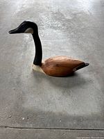 View of the wooden Canada Goose carving from one side on a concrete floor showing the bird's profile and detailed carving.
