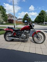 Left side profile of red cruiser motorcycle parked on paved driveway with house in background