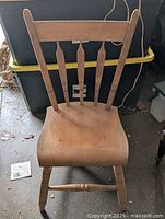 Front view of the antique wooden kitchen chair showing the backrest with four vertical spindles and contoured wooden seat.