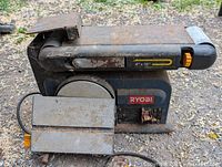 Side view of Ryobi 4x36 inch belt sander showing rust, dirt, power cord, and sanding belt.