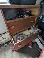 Front view of wooden chest of drawers showing open bottom drawer filled with sports cards and closed second drawer.