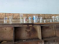 Wide angle photo showing multiple beer advertising pint glasses and mugs arranged on a shelf, includes different sizes and logos.