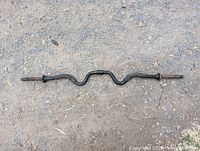 Top view of entire curling weight lifting bar on ground showing dual bends and overall shape.