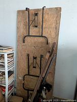 Folding table folded up and standing on its long edge, showing the underside with metal legs folded against the plywood top.