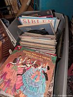 Grey plastic bucket full of vinyl LP records including visible titles and cover art.