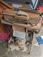Full view of the jointer planer machine mounted on the wrought iron sewing machine base with wood shavings on the floor below, showing the size and condition.