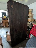 Full front view of the large solid black walnut table top standing upright showing surface wear and chip.