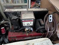 Front angle view of large red Sanborn air compressor with Dial-O-Matic control box and coiled hose.