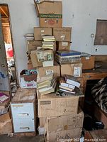 Boxes stacked with books, some labeled HarperCollins, various hardcover and paperback books visible on top and around boxes