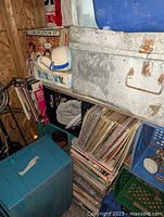 Photo showing multiple milk crates and boxes filled with stacked used 12-inch vinyl record albums along a wall in a storage area.