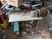 Photo showing full wood lathe mounted on wooden sewing machine table with cast iron base and motor with pulleys attached on right side.