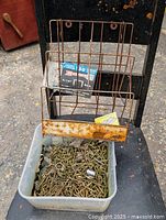 Full view of plastic container filled with used 3-inch deck screws with rusty wire rack placed on top of black chair backrest.