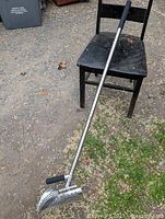 Full view of the metal sand scoop next to a chair showing the full length and handle grips.