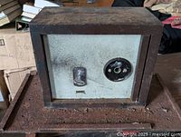 Front view of the heavy metal safe showing the key lock, combination dial, and rusted bolt-down base.
