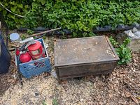 Photo of 3 red fire extinguishers in blue milk crate and metal tool chest on legs outside on ground with leaves and wood chips