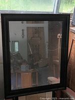 Full view of the black framed mirror reflecting a room with furniture and window.