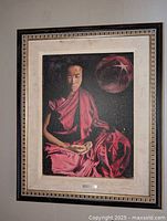 Full view of the original oil on canvas Buddha painting in red robes, framed with a cream mat and decorative frame.