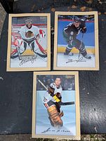 Three oversized Bee Hive hockey cards laid side by side on a dark surface showing three different players: one goaltender in a Chicago Blackhawks uniform, one skater in a Dallas Stars uniform, and one skater in a Boston Bruins uniform.