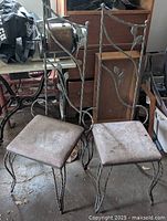 Pair of rod iron chairs with leaf motif, showing overall condition and seat cushions.