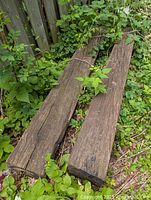 Two solid oak railway ties lying on the ground amidst greenery, showing full length and surface wear.