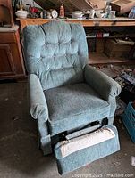 Front view of recliner chair with footrest extended. Shows greenish fabric upholstery, tufted backrest, cushioned armrests and footrest detail.