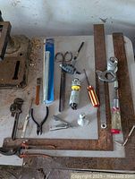 Photo showing the entire assortment of tools including two large rusty metal squares, various pliers, a wrench, scissors, a screwdriver, a hacksaw frame and other small hand tools.
