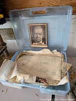 Open plastic folding tote showing multiple tattoo artist sketch sheets and vintage Winston Churchill book inside.