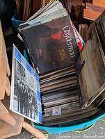 Top view of teal blue tote bin filled with vinyl LP record albums in various conditions.