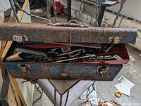 Photo of heavy rusted blue metal toolbox with lid open showing assortment of hand tools inside.