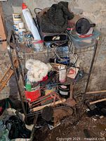 Metal wire rack shelf loaded with assorted hand tools, paint brushes, gloves, buckets with hardware, and other miscellaneous items.