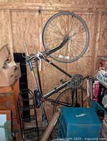 Vintage bicycle with black frame hanging on wooden wall, showing entire bike including front and rear wheels, gear system, and handlebars.