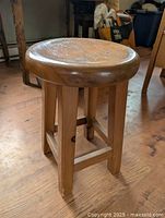 Front angle view of the solid wood round stool showing smooth round seat, four legs connected by support bars on wood floor.