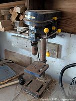 Full view of Mastercraft metal drill press including base, adjustable worktable with slots for clamping, vertical support column, and motor head with yellow lever handles.