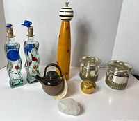 Full lot view showing all items: two painted oil and vinegar bottles with blue teapot toppers, tall yellow wooden pepper mill, two glass candle holders with metal handles, small brown ceramic teapot, gold apple decoration, and white stone.