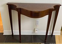 Front view of the burled wood console table showing curved front edge and four tapered legs.
