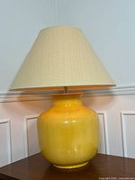 Yellow ceramic table lamp with a large beige fabric shade on a wooden table, lamp off.