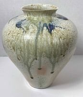 Front view of a bulbous ceramic vase with white glaze and blue-green drip pattern.