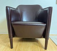 Front view of dark brown faux leather barrel chair showing overall condition and structure.