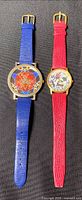 Both watches side by side on a black background, showing colorful watch faces and contrasting blue and red straps.