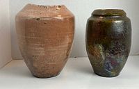 Front view of two glazed ceramic vases, left pink with flecks, right metallic colored.