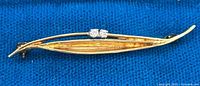 Full front view of the elongated leaf-shaped pin showing design, gold finish, and diamond placement on blue background